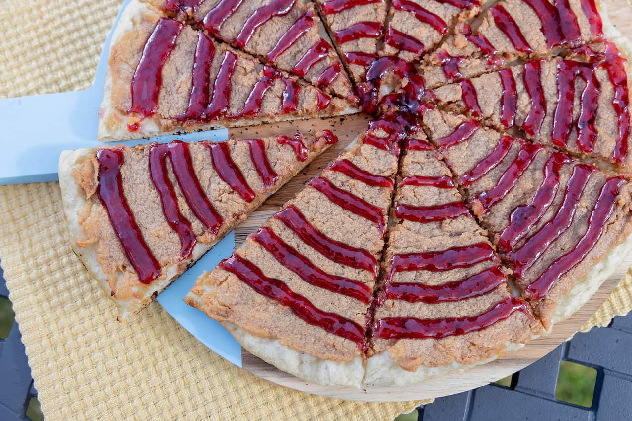 A pizza cut into 10 wedges is seen from overhead. It has a creamy-brown topping, drizzled with rings of vibrant red sauce. 