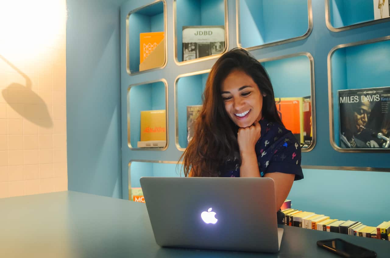 A woman smiling and working on an Apple laptop.