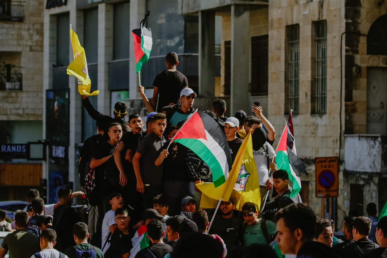 A crowd of people. Some are carrying Palestinian flags