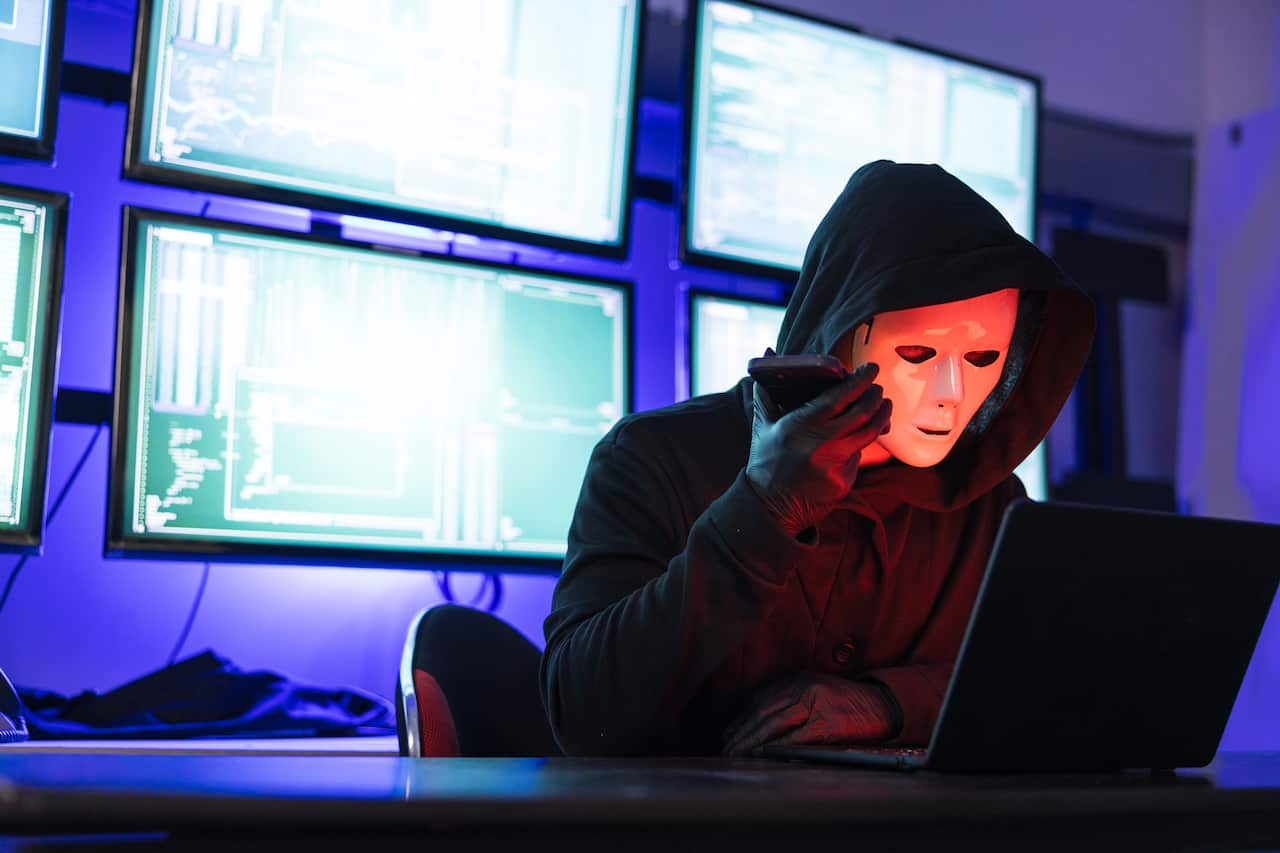 Hacker Wearing Mask using laptop computer for cyber attack and calling on cellphone, Data thief, internet attack, darknet and cyber security concept