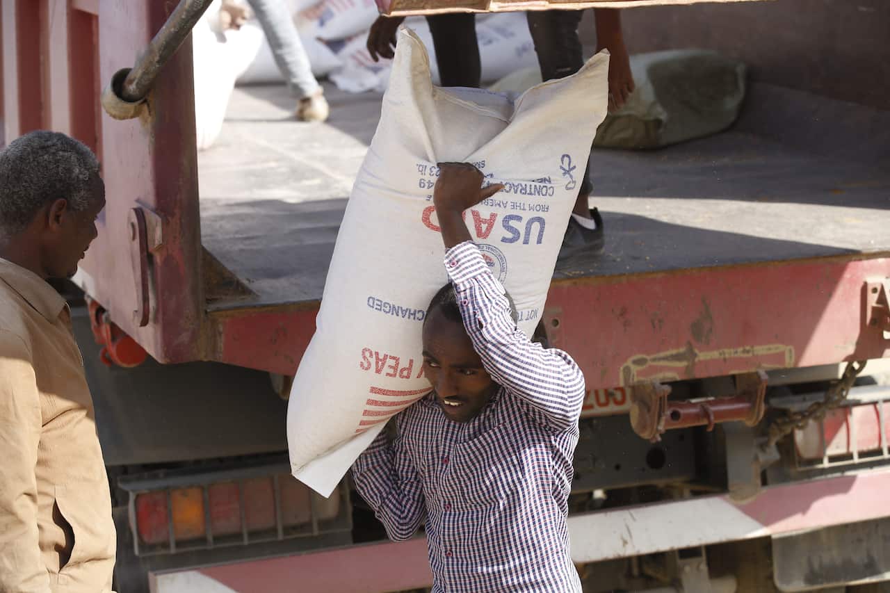 An African man is carrying a bag of peas with the USAID logo on it on his right shoulder