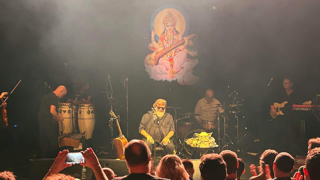 A band is performing on stage while people in the front listen.
